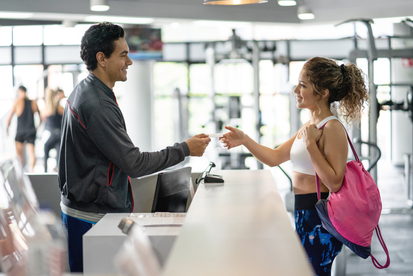 Cheerful employee at the gym handing a membership card to beautiful female customer
